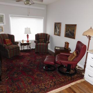 A cozy living room with armchairs, a red rug, and decorative lamps.