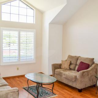 A cozy living room with a soft sofa, coffee table, and large windows letting in natural light.