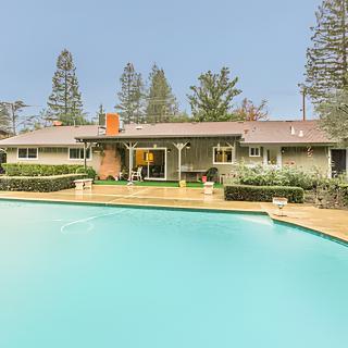 A serene backyard featuring a house with a pool and surrounding trees.