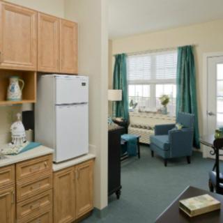 A cozy apartment interior featuring a compact kitchen and a comfortable living area with blue armchairs and large windows.