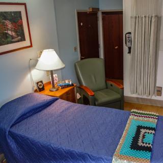 A cozy bedroom featuring a bed with blue bedding, a green chair, a bedside lamp, and decorative elements.