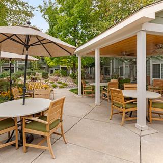 A serene outdoor patio area with tables, chairs, and umbrellas amidst lush greenery.