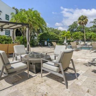 A sunny patio area with comfortable seating and a table, surrounded by lush greenery.