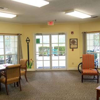 A cozy living room with various furniture and ample natural light from large windows.