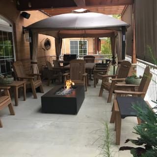 A cozy outdoor patio setup featuring wooden chairs, a modern fire pit, and a protective canopy for comfortable gatherings.