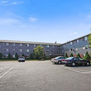 An apartment complex with a parking lot in front, featuring several parked cars under a clear blue sky.