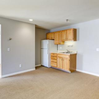 A minimalist apartment kitchen with wood cabinets and a refrigerator.