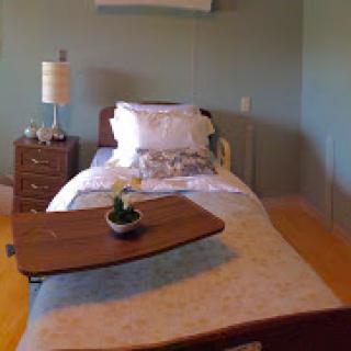 A cozy bedroom featuring a simple bed, bedside lamp, and a wooden table.