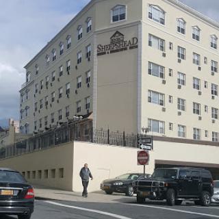 A view of a hotel building from the street, with cars parked nearby.