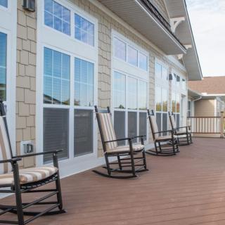 A row of rocking chairs on a spacious deck, lined with large windows.