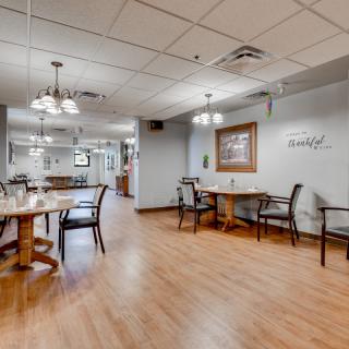 A well-lit dining area with wooden tables and chairs on a hardwood floor.