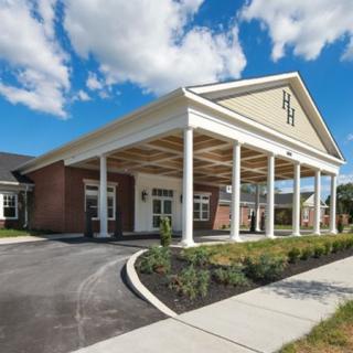 A modern building entrance with columns and a landscaped driveway under a cloudy sky.