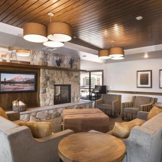 A cozy and modern living room featuring a stone fireplace, comfortable seating, and a wooden ceiling.