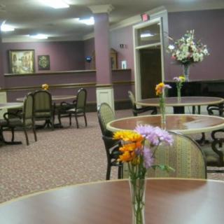 A cozy dining area with tables, chairs, and floral decorations on a carpeted floor.
