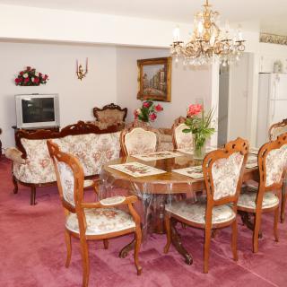 A vintage-style living room with a connected dining area, featuring ornate furniture, a chandelier, and traditional decor.