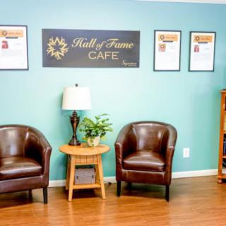 A cozy cafe waiting area with leather chairs, a lamp, and framed decorations on the wall.