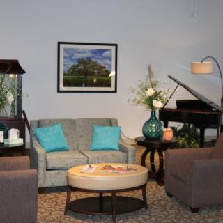 A cozy living room with a sofa, armchairs, and a piano, accented by decorative elements and artwork.