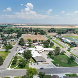 An aerial view of a residential area showcasing green spaces and nearby agricultural fields under a partly cloudy sky.