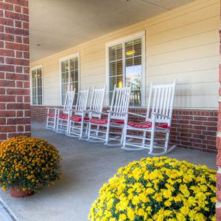 A cozy porch features white rocking chairs with vibrant potted flowers.