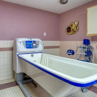 A specialized bathtub in a healthcare facility room with tiled flooring and wall decorations.