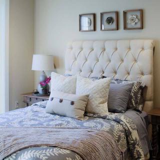 A cozy and elegantly designed bedroom with a tufted headboard, decorative pillows, and framed artwork.