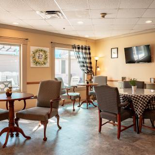 A cozy dining area with tables, chairs, and a wall-mounted television, featuring soft lighting and checkered curtains.
