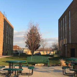 A campus courtyard with outdoor seating between two buildings on a clear day.