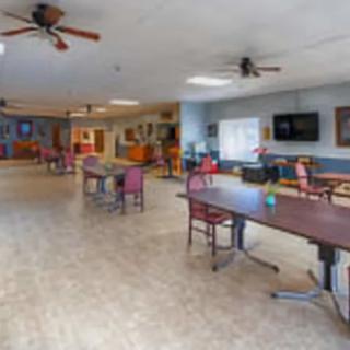 A spacious indoor room featuring tables, chairs, ceiling fans, and a television.