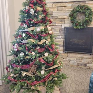 A beautifully decorated Christmas tree with ribbons, ornaments, and a wreath near a cozy fireplace.