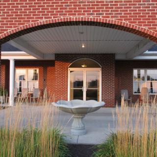 An elegant brick building entrance with a central fountain surrounded by tall grasses.