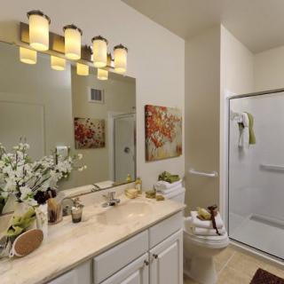 A modern bathroom featuring a large mirror, single sink, and a shower area with elegant lighting and simple decor.