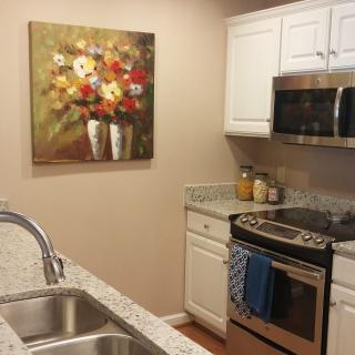 A modern kitchen with a floral painting, stainless steel appliances, and granite countertops.