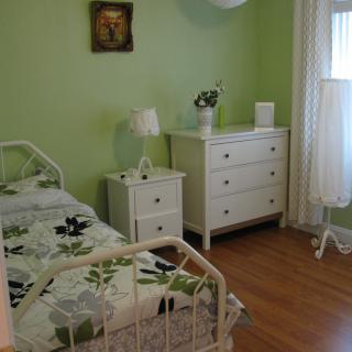 A cozy bedroom with green walls, featuring a single bed, a dresser, and a nightstand.
