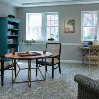 A cozy and organized living room with a table and chairs, a bookshelf, and large windows.