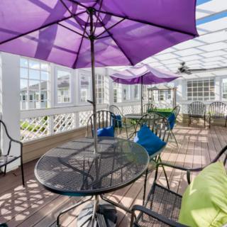 A sunlit patio featuring glass tables and chairs under vibrant purple umbrellas.