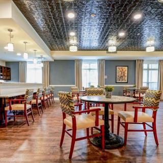 A spacious dining area with round tables and patterned chairs, featuring a decorative ceiling and wooden flooring.