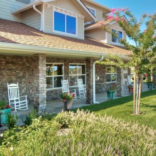 A charming house with a stone exterior features a cozy porch equipped with white rocking chairs, surrounded by a well-maintained garden.