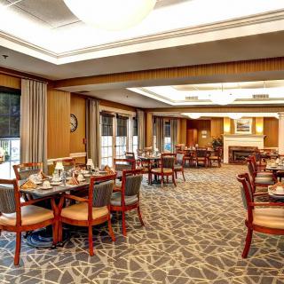 An elegantly designed restaurant dining area with neatly arranged tables and chairs, featuring warm lighting and carpeted floors.