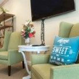A cozy living room setup with green chairs, a decorative pillow, and a floral arrangement on a side table.