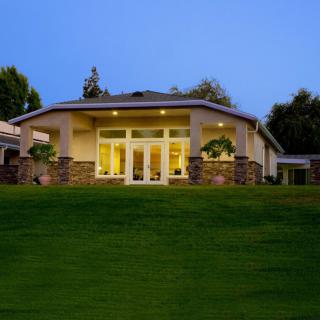 A well-lit house with large windows and a manicured lawn during the evening.
