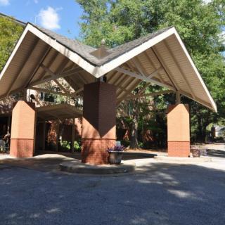 A building entrance with a distinctive roof structure, surrounded by trees.