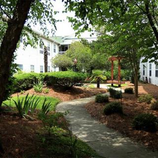 A serene garden with a winding pathway surrounded by lush greenery and benches, adjacent to a residential building.