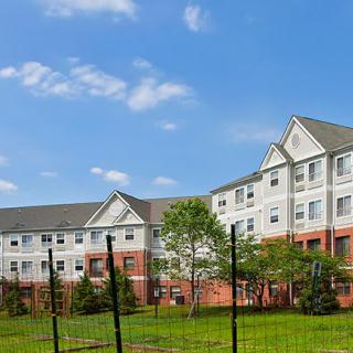 A residential apartment building with a well-kept lawn and surrounding trees under a clear blue sky.