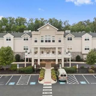 A large residential building with a central entrance, surrounded by a parking lot and trees.