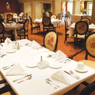 An elegantly set dining area in a restaurant with white tablecloths and ornate chairs.