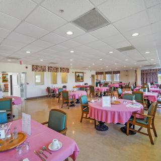 A spacious dining room with multiple tables covered in pink tablecloths, set for guests.