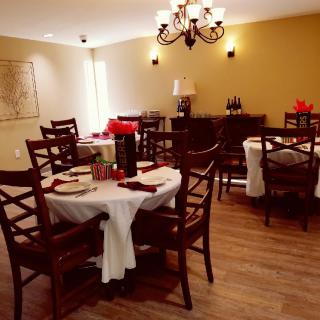 A cozy dining room with elegantly set tables and wooden chairs under a chandelier.