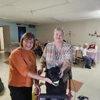 Two women pose with a dog during a community gathering.