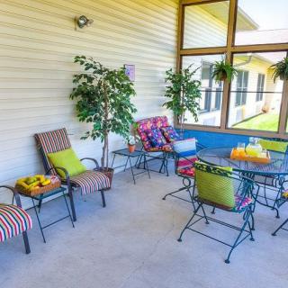 A cozy patio area with colorful cushioned chairs and a table, surrounded by lush green plants.