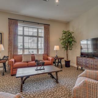 A cozy living room with a sofa, coffee table, and television, featuring warm decor and ample natural light.
